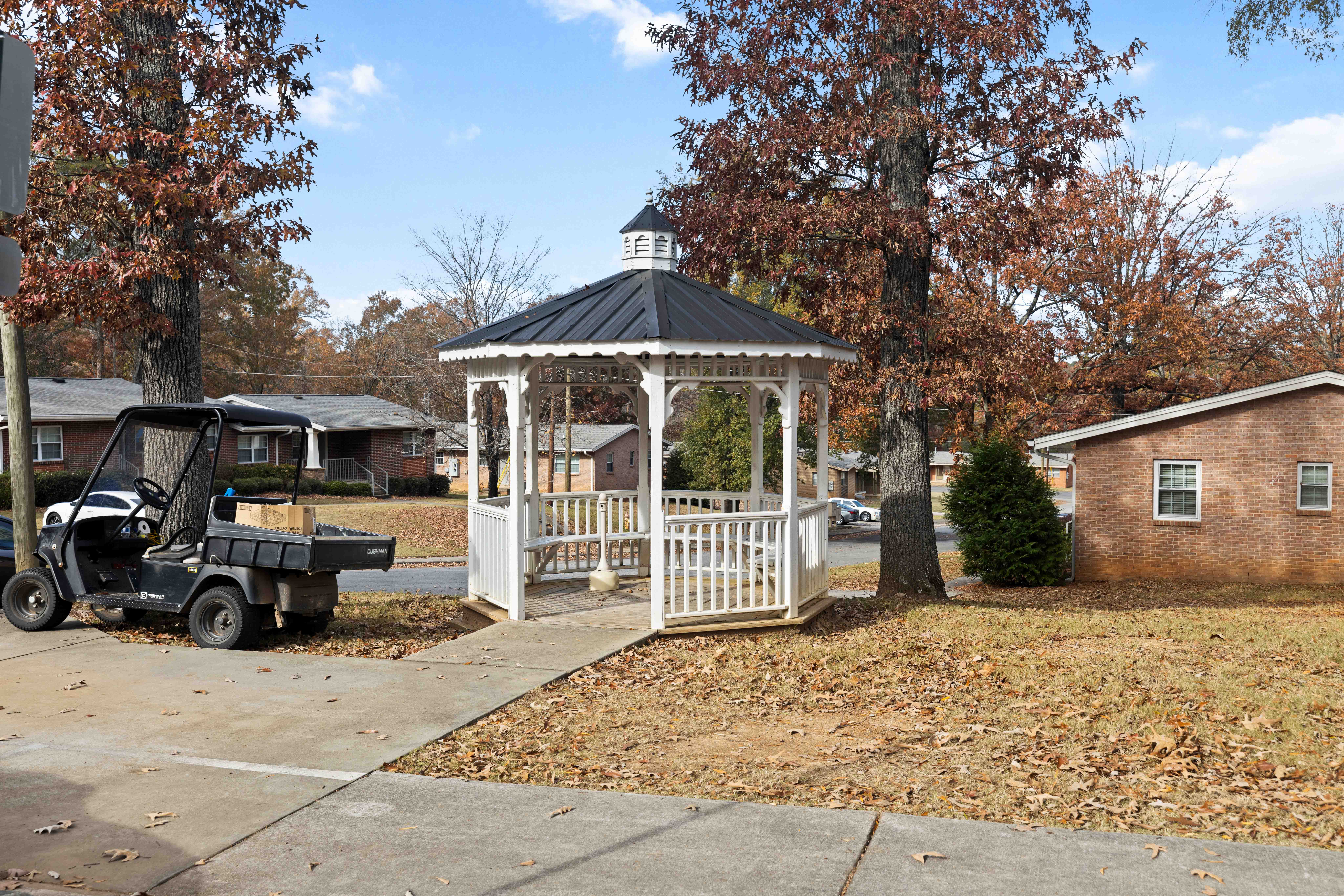 A gazebo is in the middle of a yard with a black golf cart behind it.